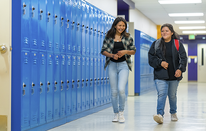two smiling students walking in school hallway